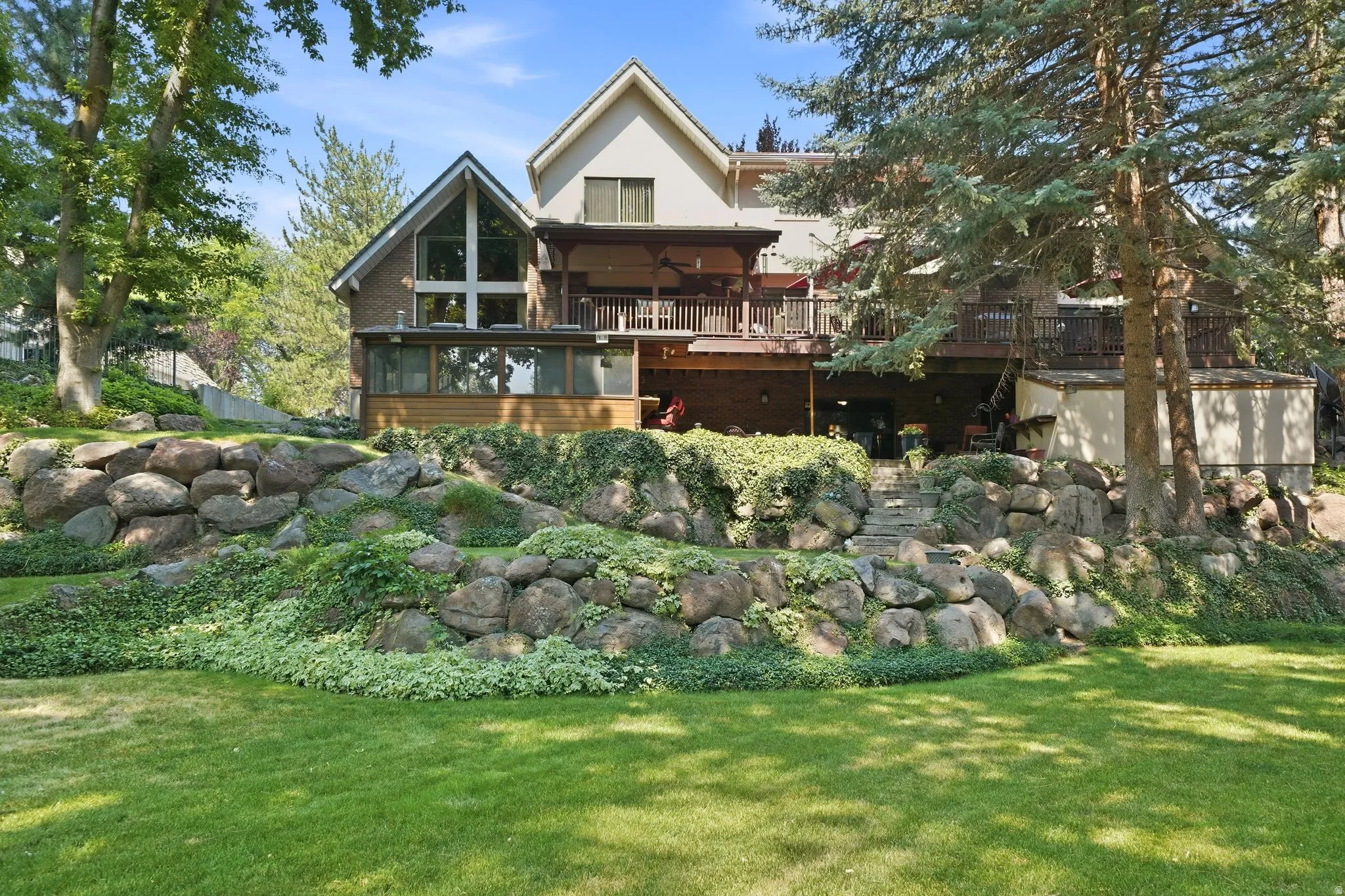 Expansive terraced backyard featuring a manicured lawn, established trees, and natural rock landscaping
