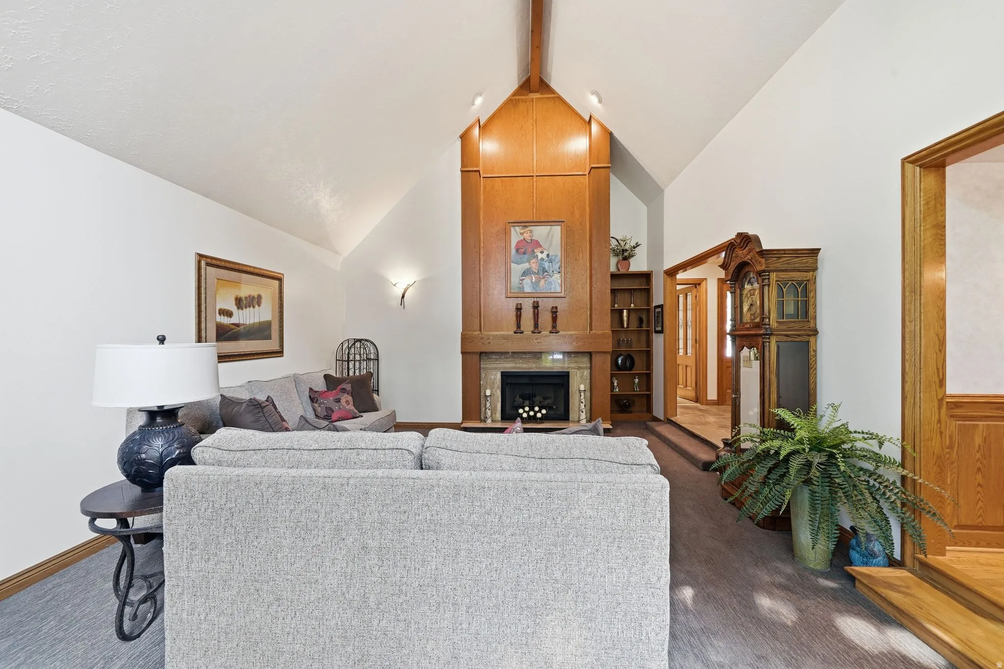 Living area featuring vaulted ceilings, a wood-paneled fireplace surround with a mantel, an integrated fireplace unit, and recessed lighting