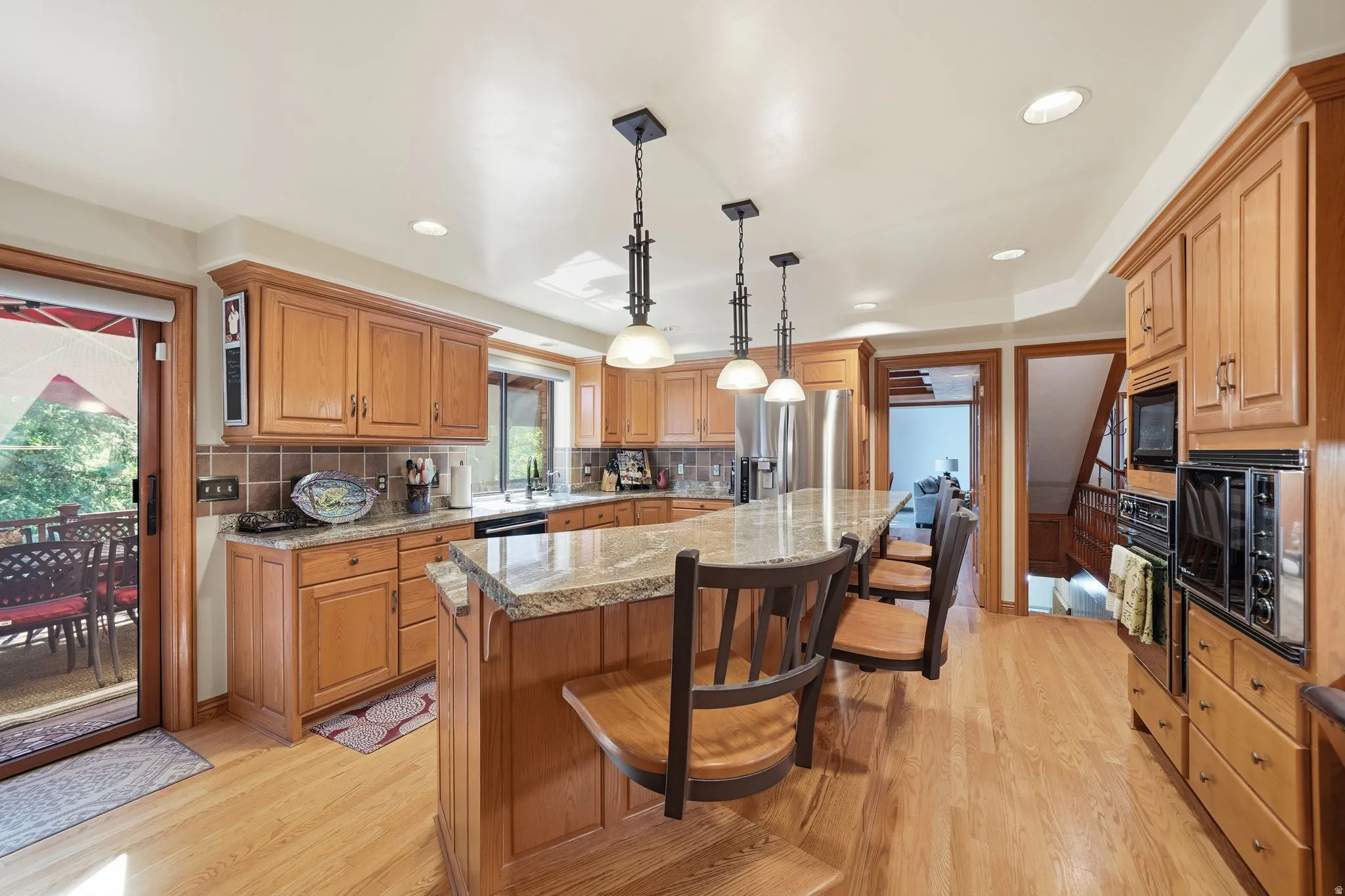 Kitchen featuring wood cabinetry, stone countertops, stainless steel appliances, a center island with pendant lighting, and wood-finish flooring