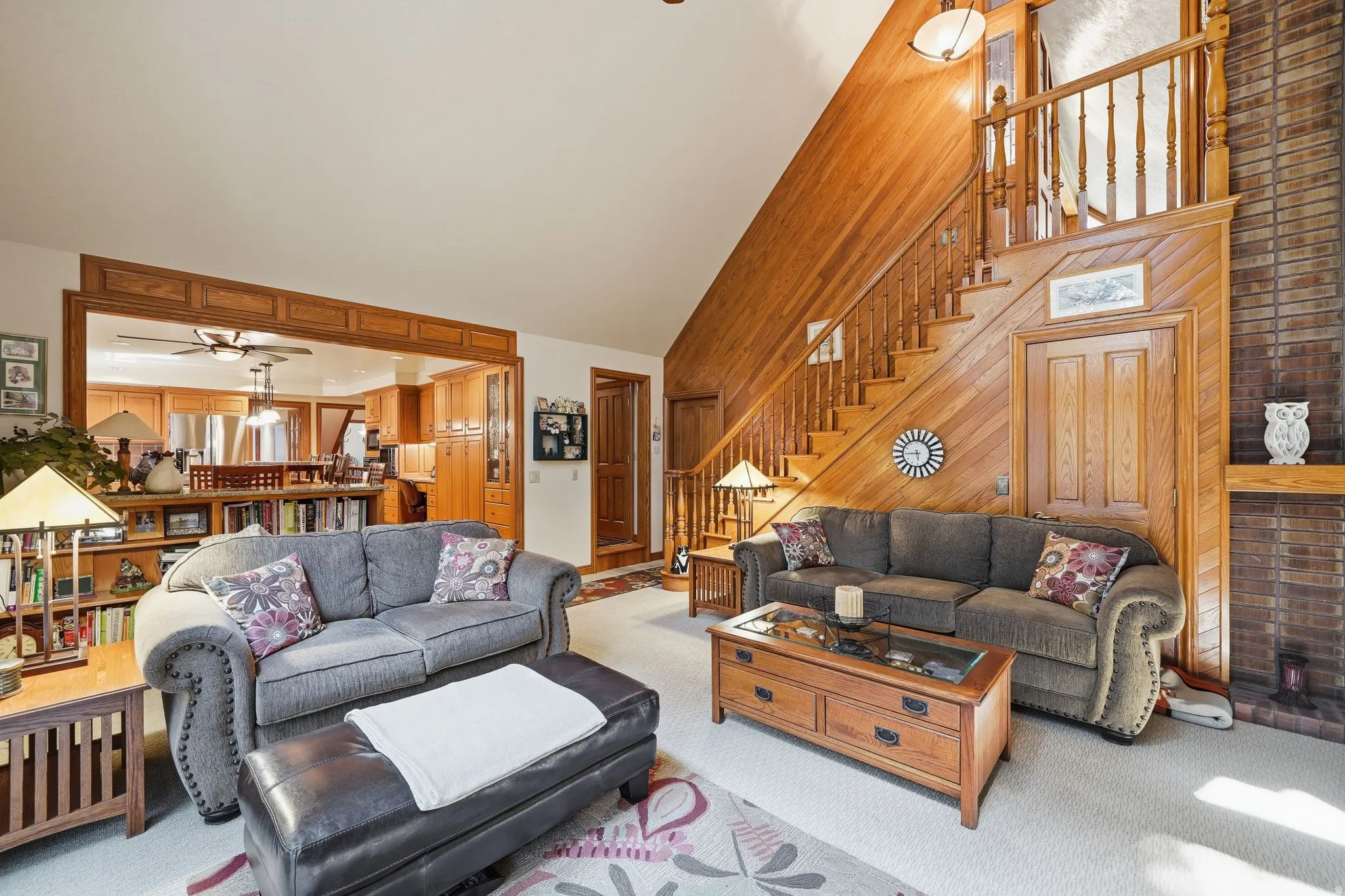 Spacious living area featuring a prominent wood-finish staircase, vaulted wood-finish ceiling, and an open concept archway to the kitchen