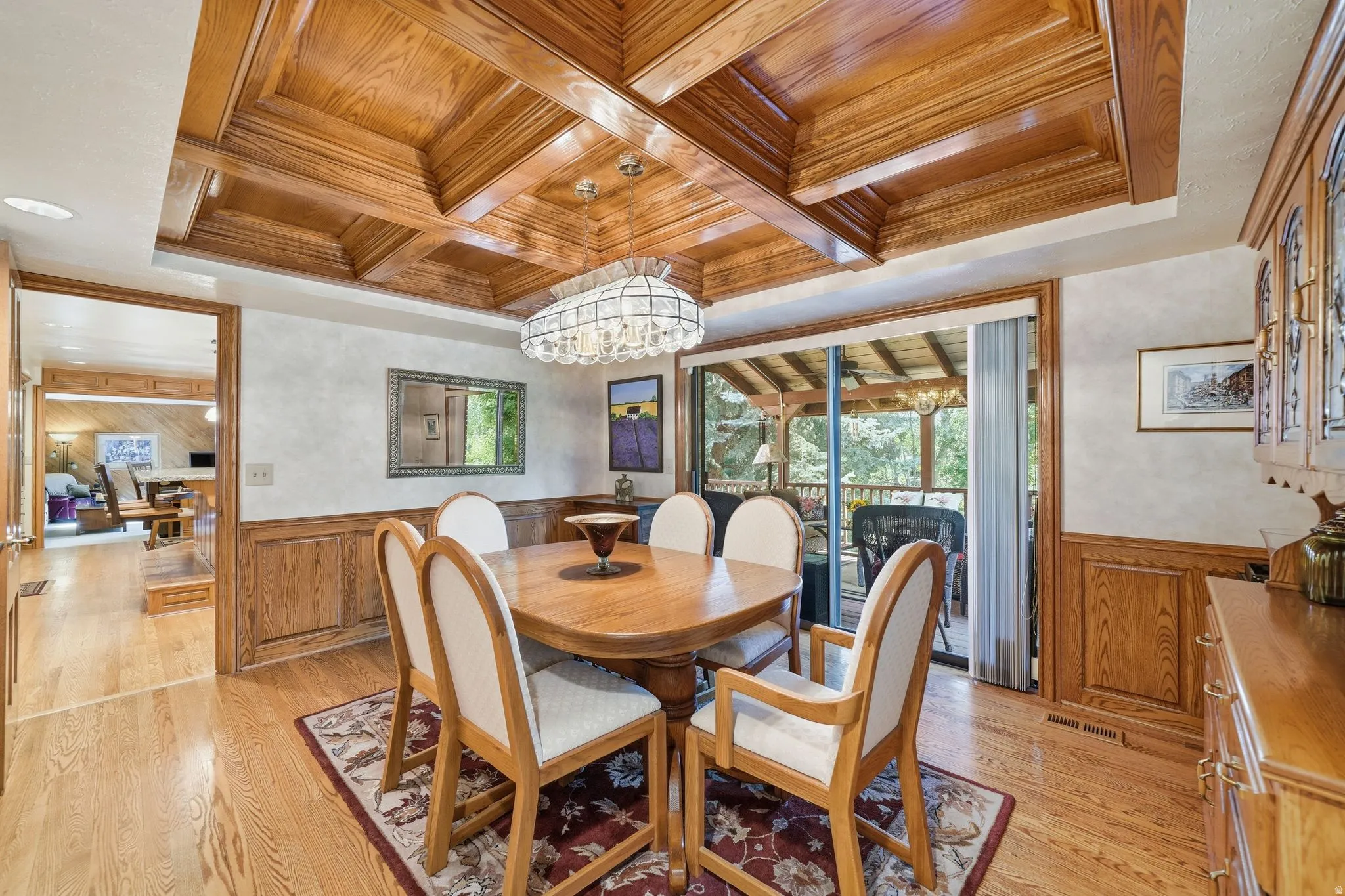Formal dining space featuring a coffered wood ceiling, wood-finish flooring, wainscoting, and a sliding glass door opening to an outdoor patio