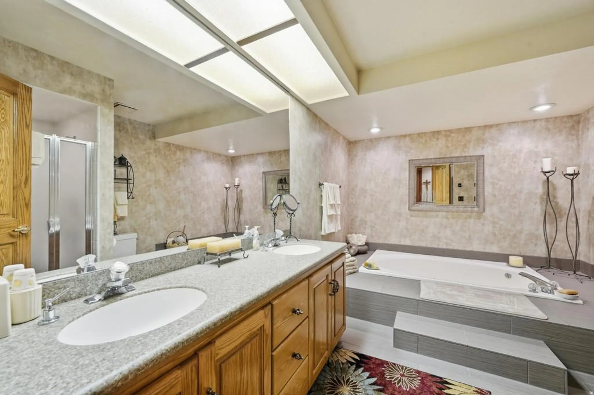 Bathroom featuring a dual vanity with a granite-finish countertop, wood cabinetry, an integrated soaking tub, and a separate shower enclosure