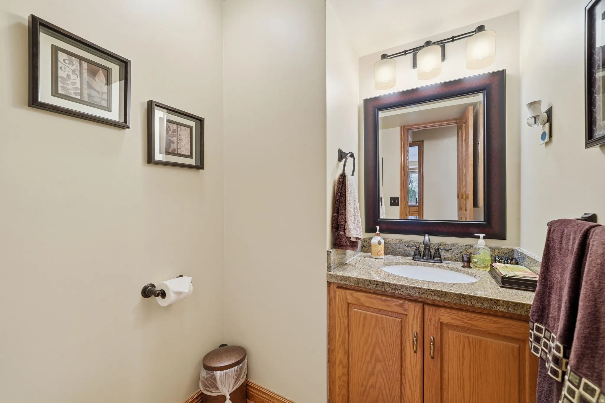 Vanity with integrated sink, stone-finish countertop, wood cabinetry, and framed mirror with three-bulb vanity lighting