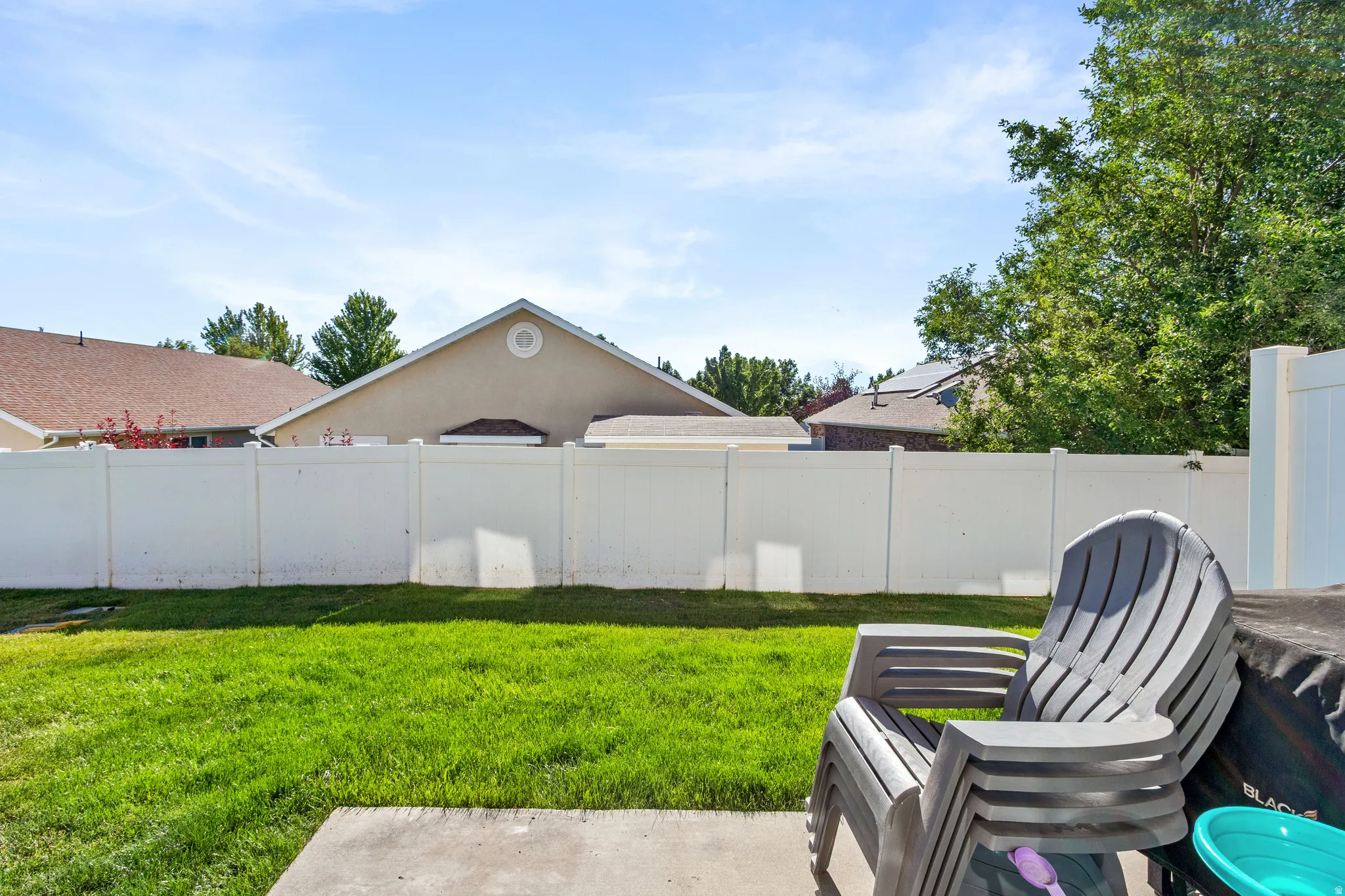 Lawn with concrete patio area, surrounded by a white privacy fence