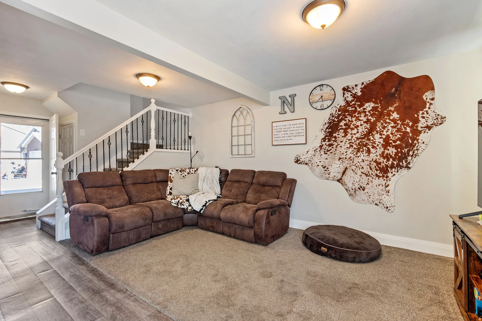 Open-concept living area featuring a carpeted floor, light gray wall paint, and a staircase with white balusters and wrought iron spindles