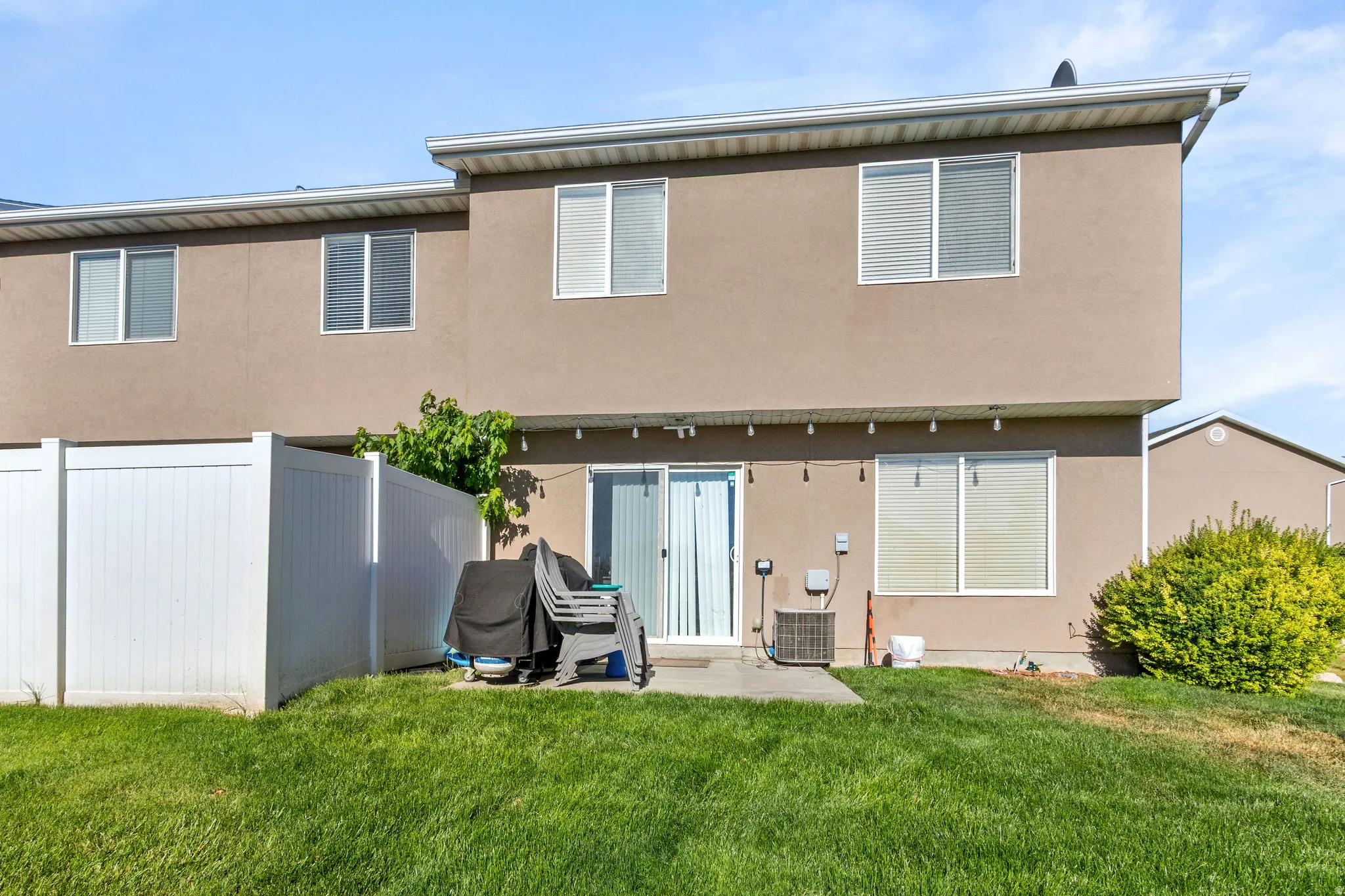 Expansive backyard featuring a manicured lawn, a concrete patio, and a white privacy fence