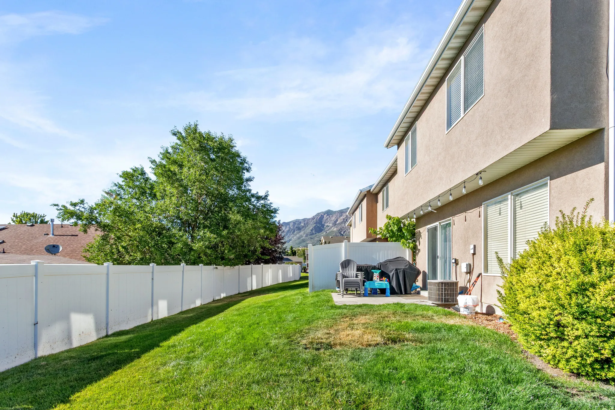 Expansive grassy yard with a concrete patio, featuring a white privacy fence and mature landscaping