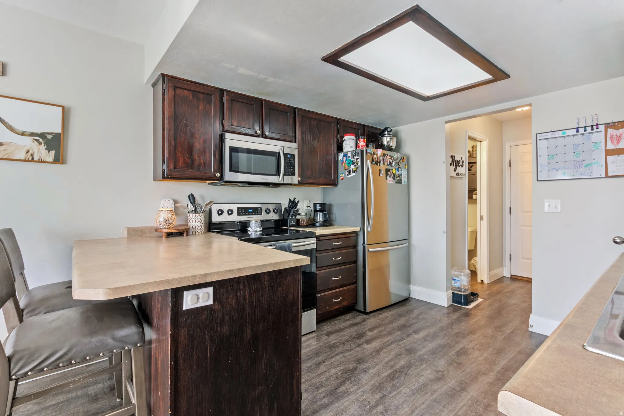 Kitchen featuring wood-finish flooring, dark wood cabinetry, a built-in microwave, and a skylight