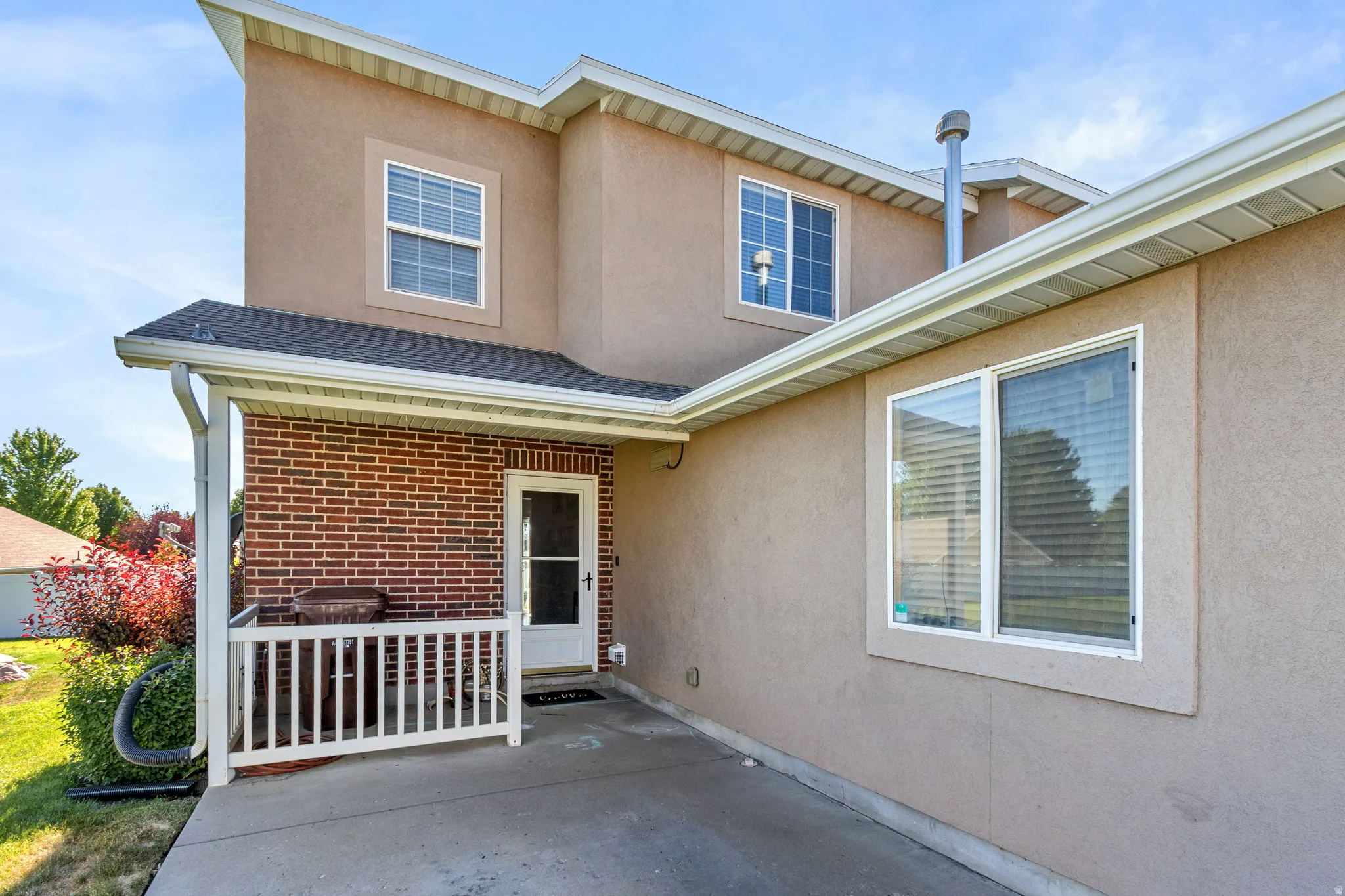 Concrete patio with brick accent wall, white railing, and stucco exterior