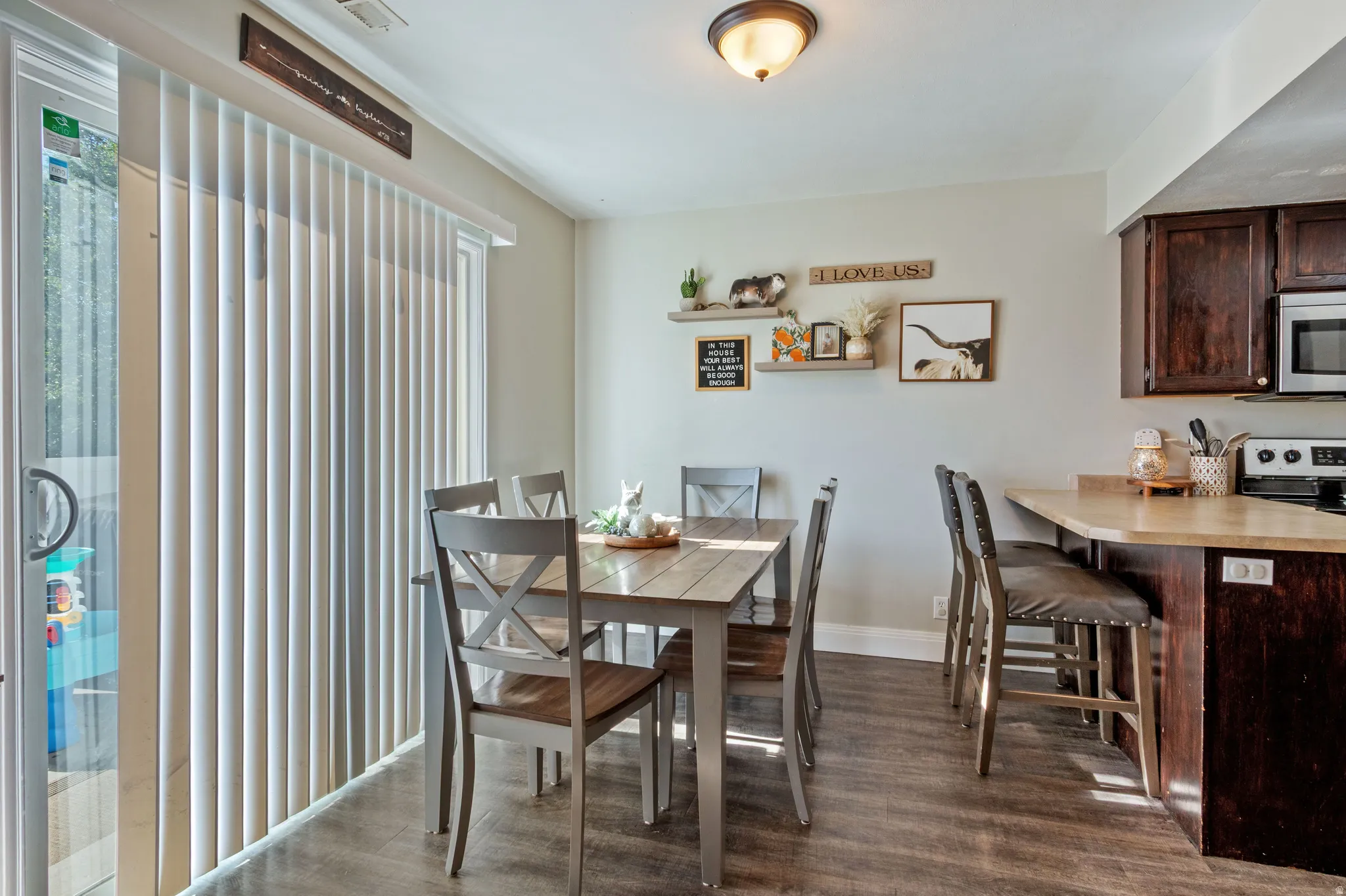 Dining area featuring wood-finish flooring, a sliding glass door with vertical blinds, and a kitchen pass-through with counter seating