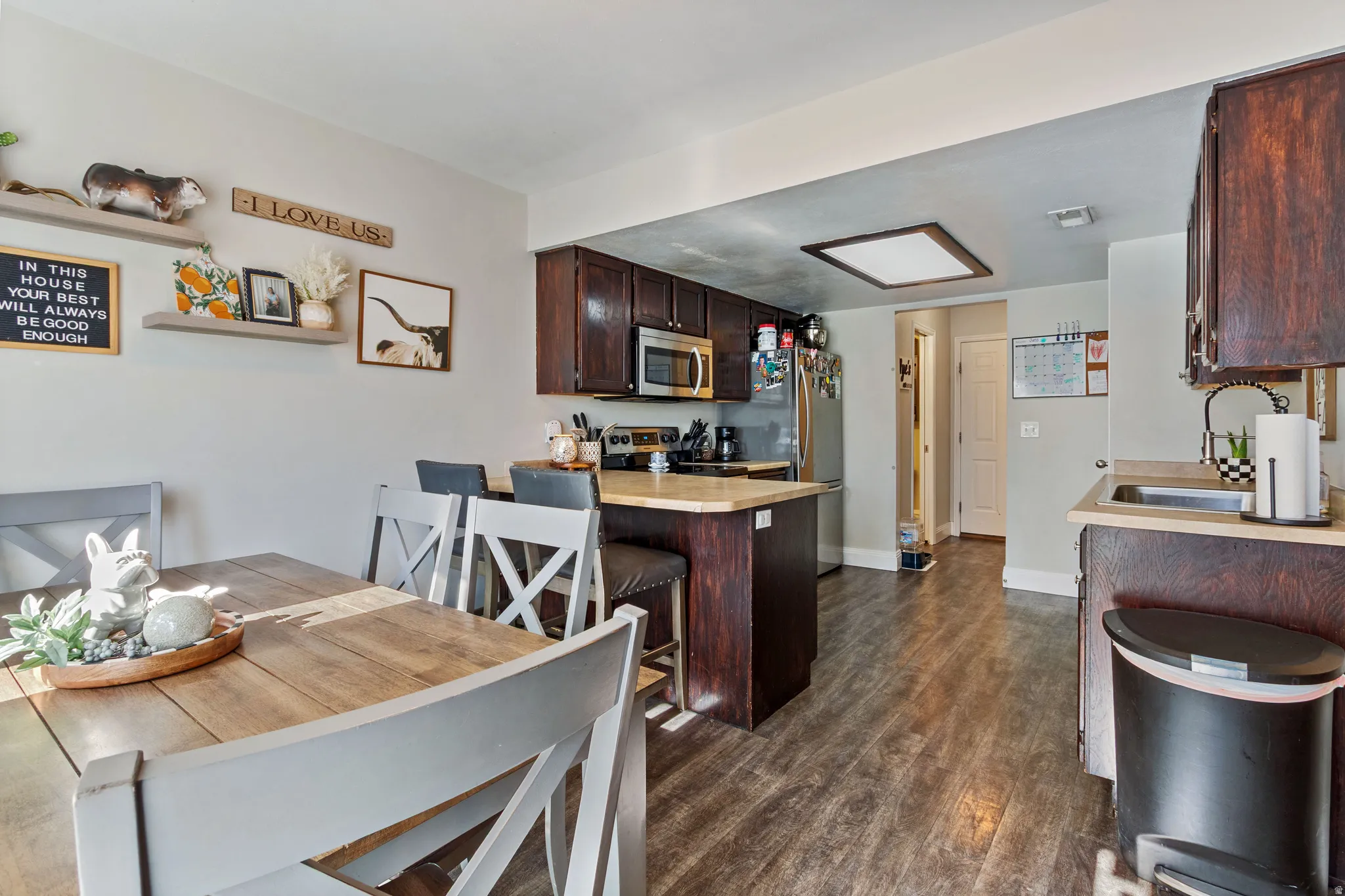 Kitchen featuring dark wood cabinetry, stainless steel appliances, a center island with bar seating, and light-toned countertops