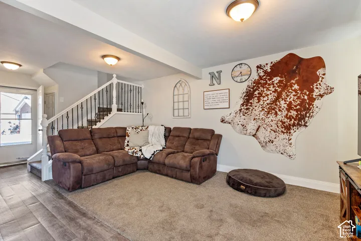 Open-concept living area featuring a carpeted floor, light gray wall paint, and a staircase with white balusters and wrought iron spindles