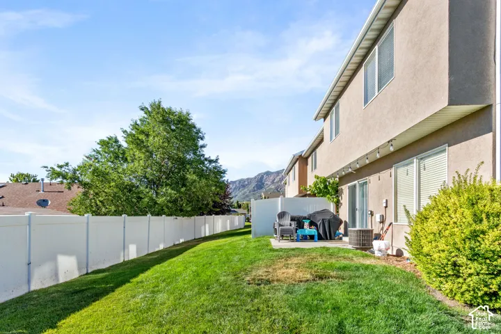 Expansive grassy yard with a concrete patio, featuring a white privacy fence and mature landscaping