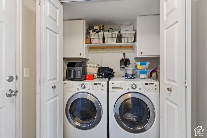 Dedicated laundry area featuring white bi-fold doors, upper cabinetry, an open shelf, and white front-load appliances