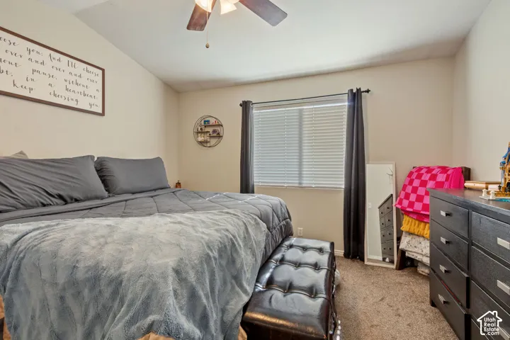 Spacious bedroom featuring neutral wall tones, textured carpet, and a ceiling fan with integrated lighting