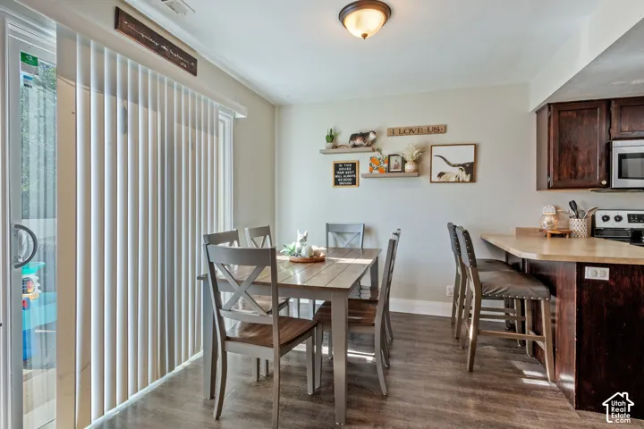 Dining area featuring wood-finish flooring, a sliding glass door with vertical blinds, and a kitchen pass-through with counter seating