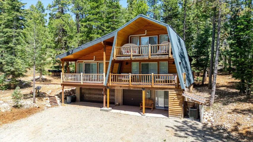 Rustic wood-sided chalet featuring a multi-level design with two balconies, a sloped metal roof, and a two-car garage