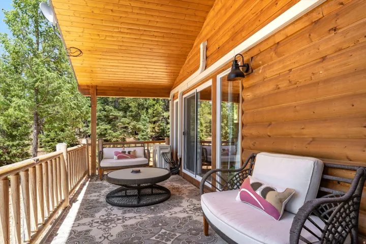 Covered porch featuring natural wood log siding and ceiling, sliding glass doors, a decorative outdoor rug, and a rustic wood railing