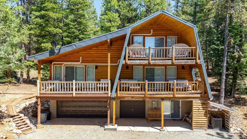 Wood-sided A-frame structure featuring a dark-toned roof, multiple sliding glass doors, two upper-level balconies with wood railings, and a lower-level covered patio area