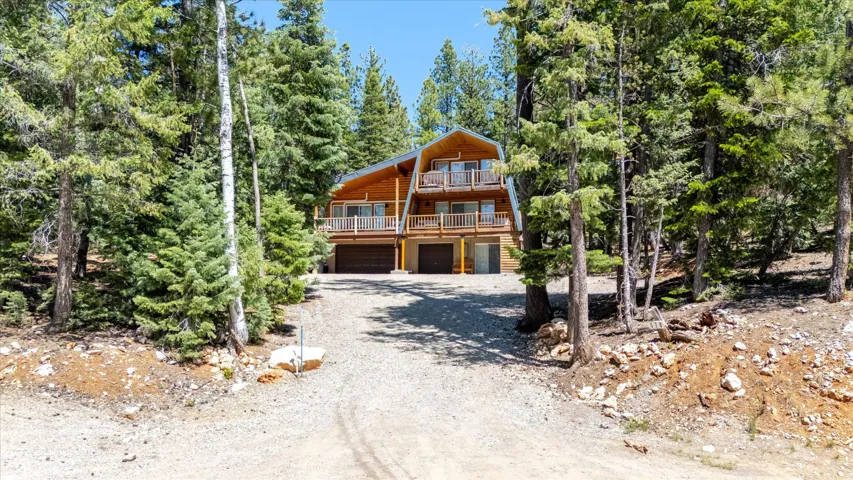 Wood-sided A-frame residence featuring multiple balconies and a gravel driveway