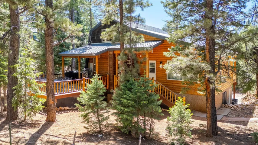 Log-sided residence featuring a covered deck with wood railings, an exterior staircase, a metal roof, and surrounding mature pine trees