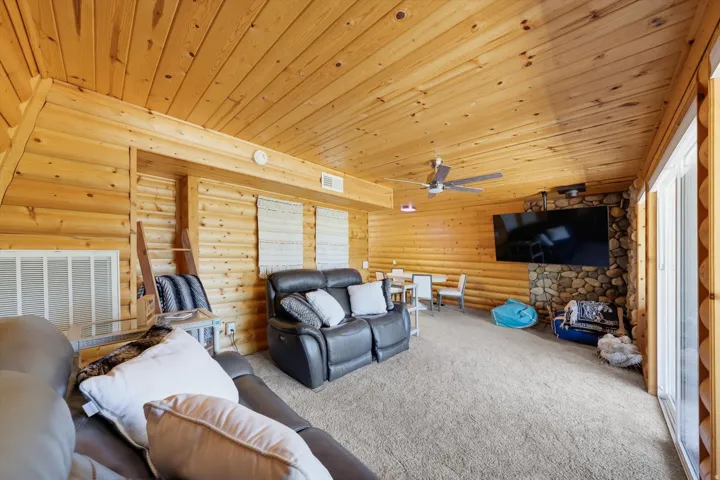 Room featuring natural wood walls and ceiling, a stone-clad accent wall, a ceiling fan, and carpet flooring