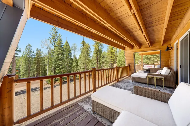 Expansive covered deck with exposed wood beam ceiling, wood-finish flooring, and natural wood railing