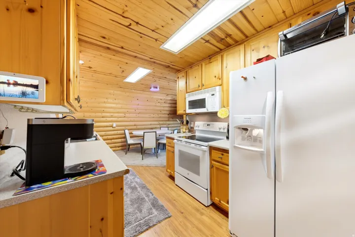Kitchen featuring wood-finish flooring, natural wood cabinetry, white appliances, and a built-in microwave