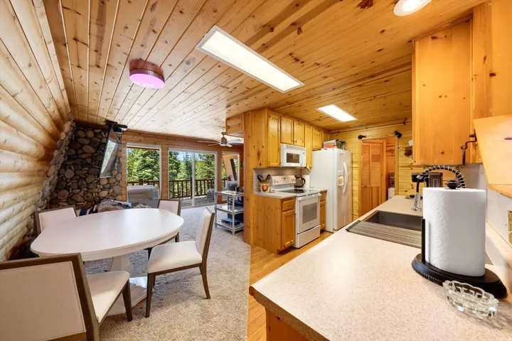 Wood-paneled ceilings with recessed lighting, stone-clad fireplace, and sliding glass door leading to an outdoor deck