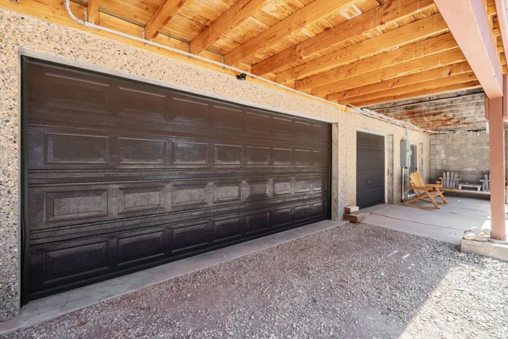 Two dark paneled garage doors set into a concrete exterior with exposed wood ceiling beams