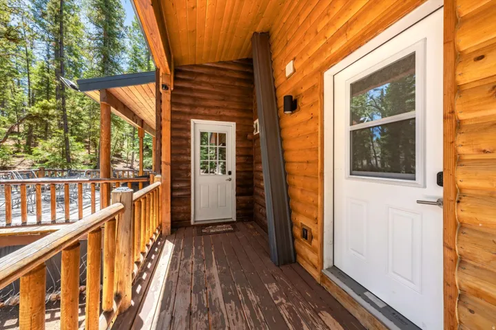 Expansive wood-finish deck with log railings and a partial overhang, featuring two white exterior doors with glass inserts and black wall-mounted lighting