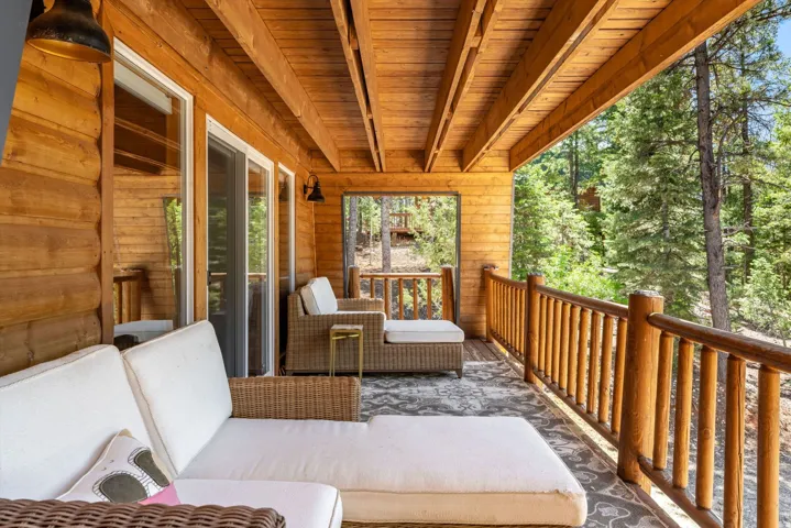 Spacious wood-paneled balcony featuring a wood-beam ceiling, natural wood railing, and multiple glass sliding doors