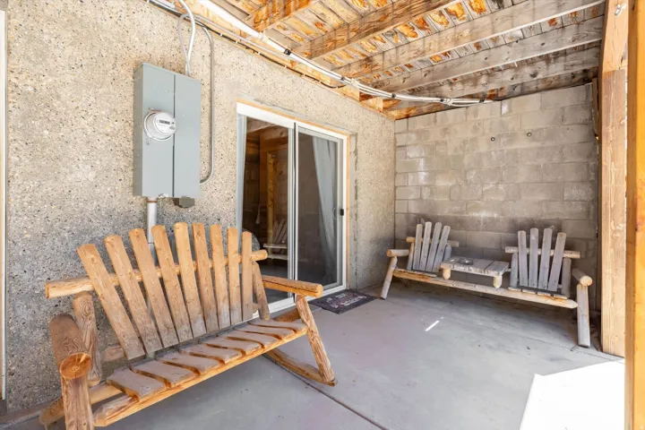 Covered patio area featuring concrete flooring, a stucco-finish exterior wall, and an exposed wood beam ceiling