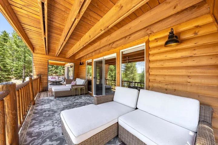 Expansive covered deck featuring a natural wood ceiling, wood-finish walls, log railing, and multiple glass sliding doors