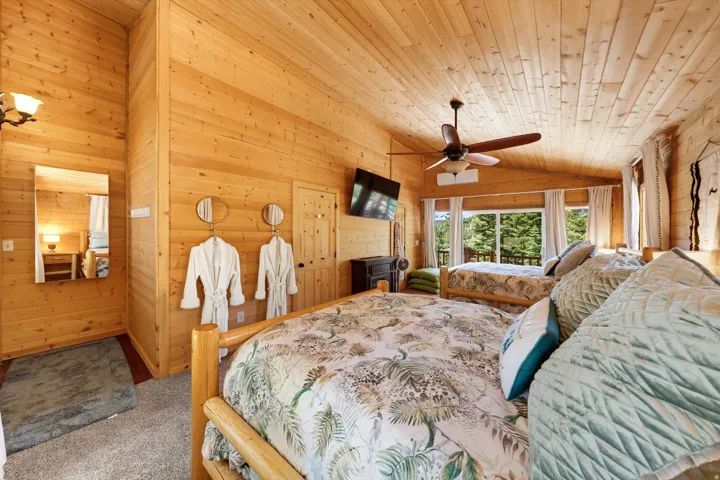 Wood-paneled room featuring a vaulted ceiling with a ceiling fan, two wood-frame beds, and a large window overlooking trees