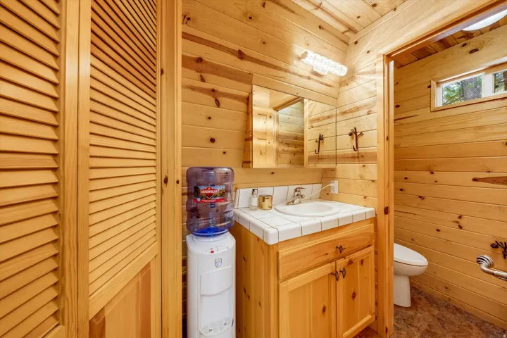 Bathroom featuring wood-paneled walls and ceiling, a vanity with a tiled countertop, and a built-in louvered door