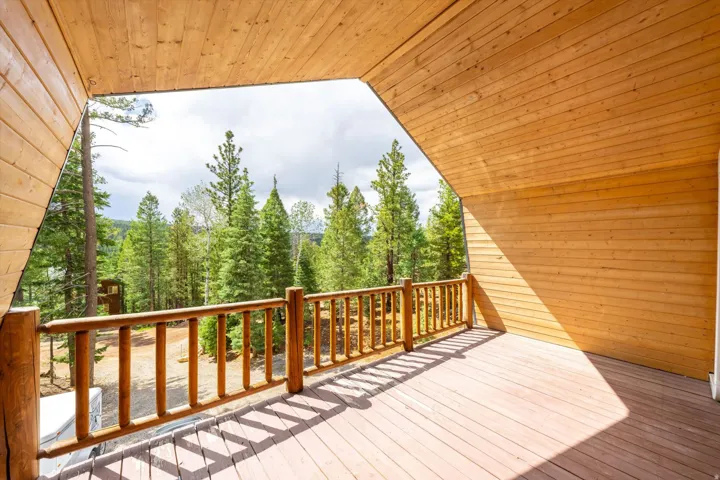 Expansive wood deck featuring a natural wood railing and a sloped wood-paneled ceiling, overlooking a dense evergreen tree line