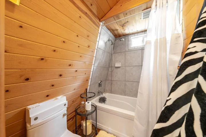 Bathroom featuring wood paneling, tiled tub surround, and a compact window