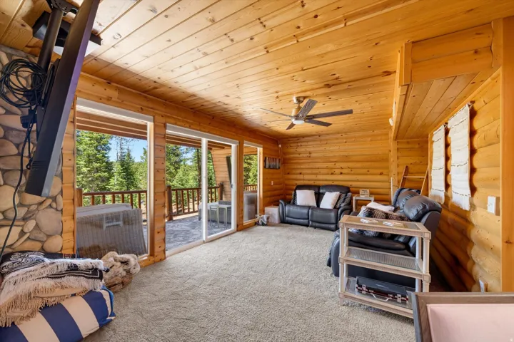 Expansive room featuring wood-paneled walls and ceiling, a ceiling fan, plush carpeting, and multiple sliding glass doors opening to an exterior deck