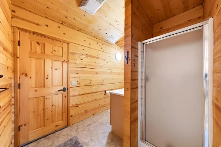 Vertical wood-paneled walls and sloped ceilings define this space, featuring a six-panel wood door with dark hardware