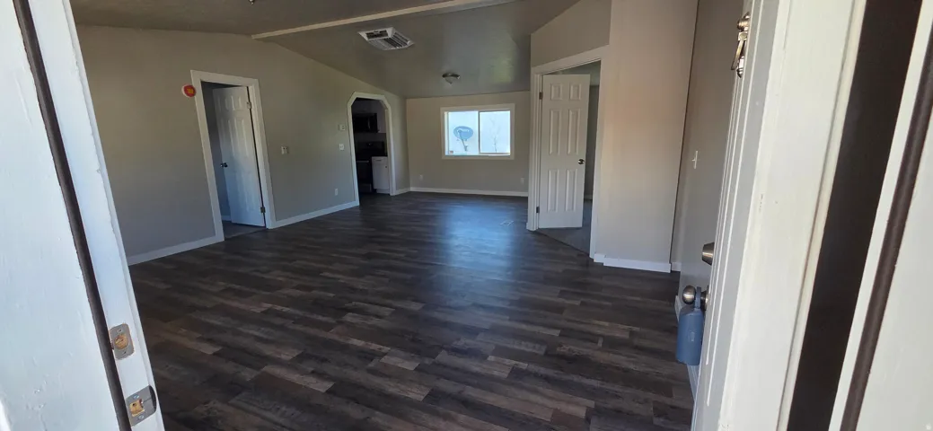 Spacious room featuring vaulted ceilings, wood-finish flooring, light gray wall tones, and white trim