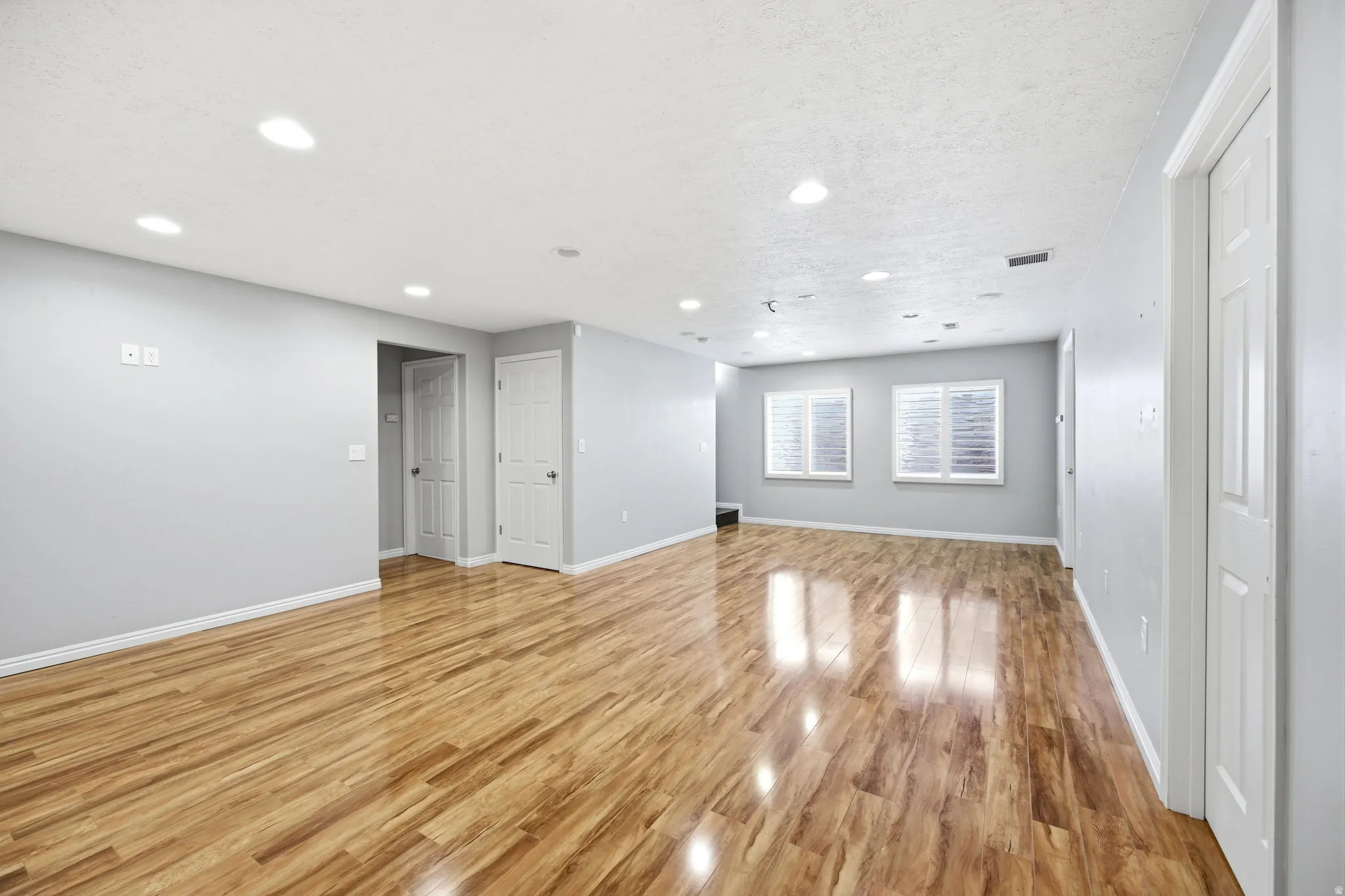 Spacious room featuring wood-finish flooring, light gray walls, recessed lighting, and white baseboards