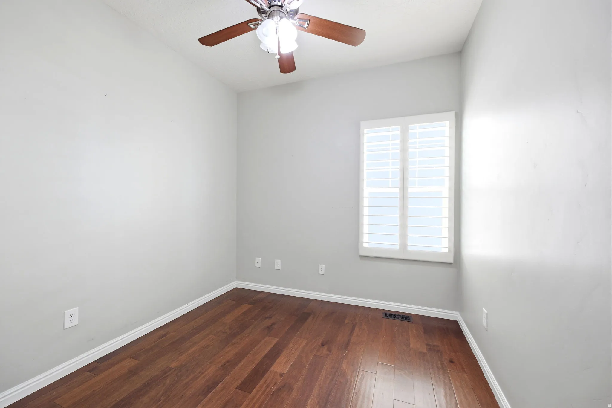 Room featuring wood-finish flooring, white baseboards, and a ceiling fan with light fixture