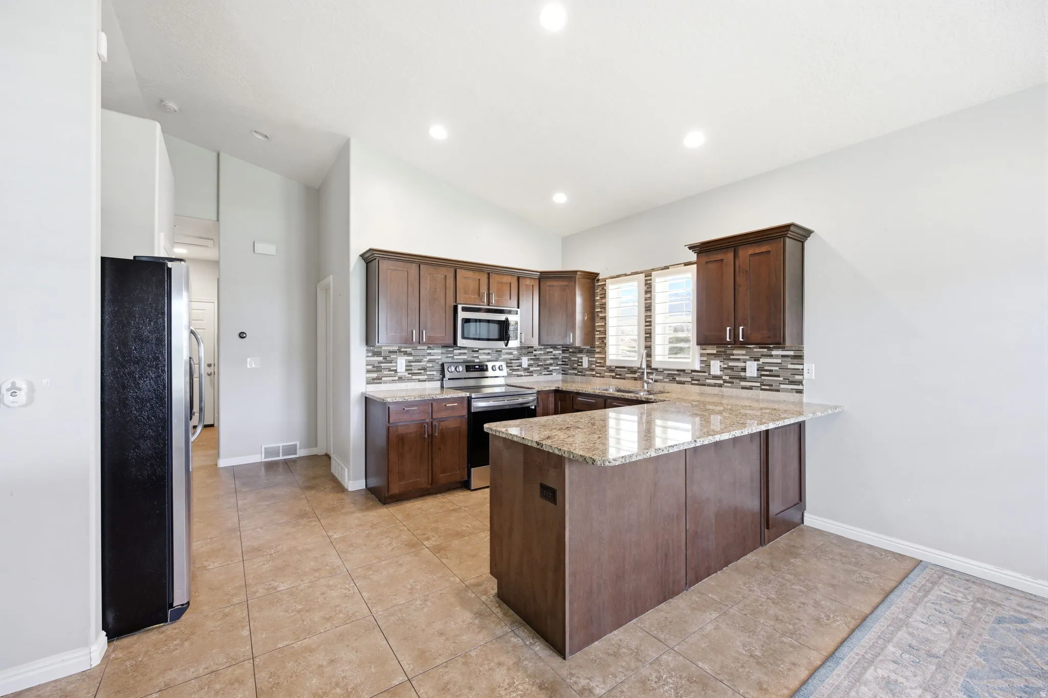 Kitchen featuring wood cabinetry, stainless steel appliances, granite countertops, tile backsplash, and recessed lighting