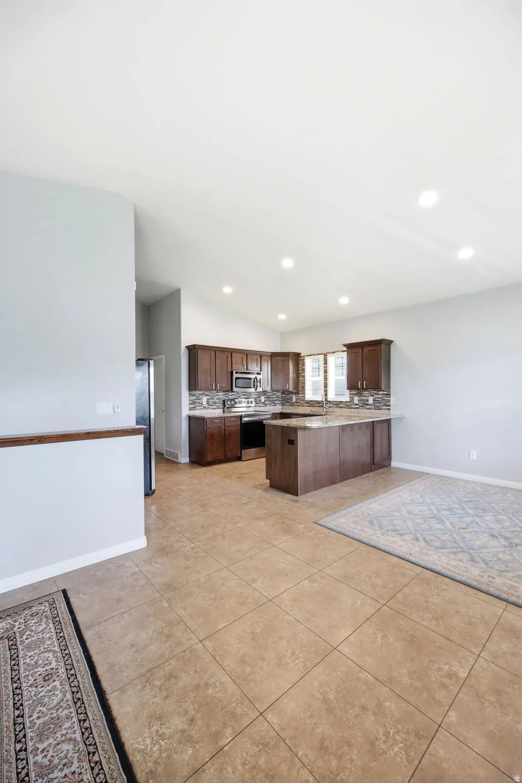 Open-concept kitchen featuring wood cabinetry, stainless steel appliances, a stone-finish backsplash, and an island with bar seating