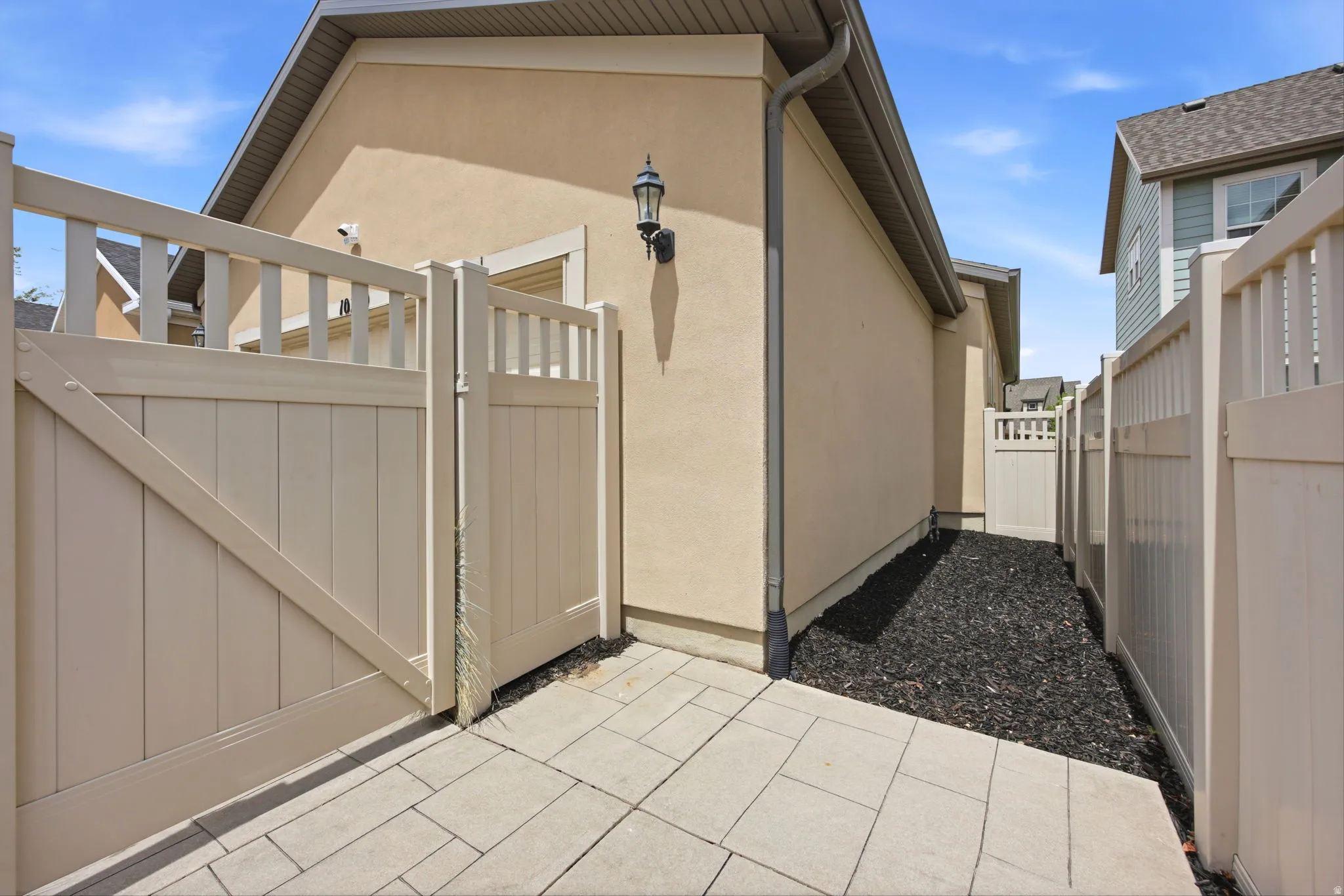 Private side yard featuring paver stones, a light-colored stucco exterior, and a decorative outdoor light fixture