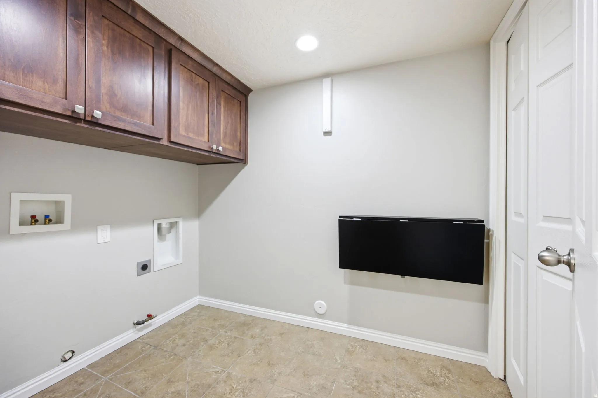 Laundry area featuring dark wood-finish cabinetry, tile flooring, and a wall-mounted folding surface