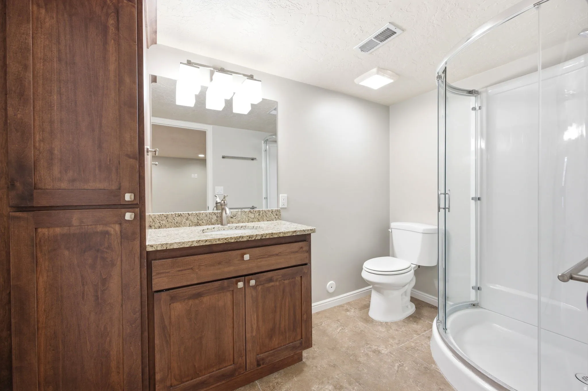 Bathroom featuring a wood-finish vanity with a granite-style countertop, undermount sink, and wall-mounted mirror