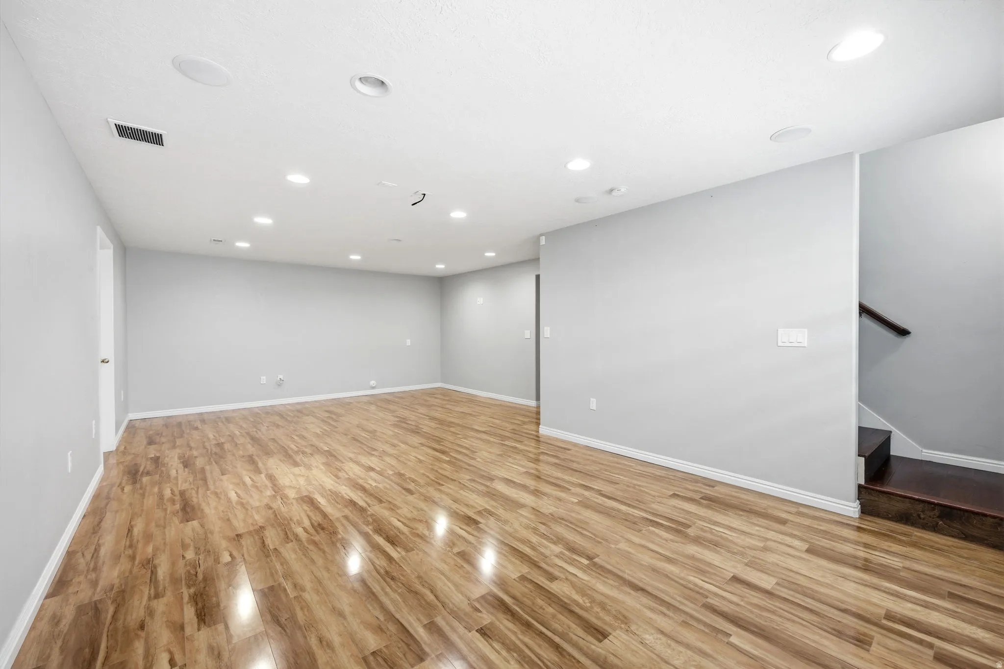 Expansive open room featuring wood-finish flooring, recessed lighting, light gray walls, and white baseboards
