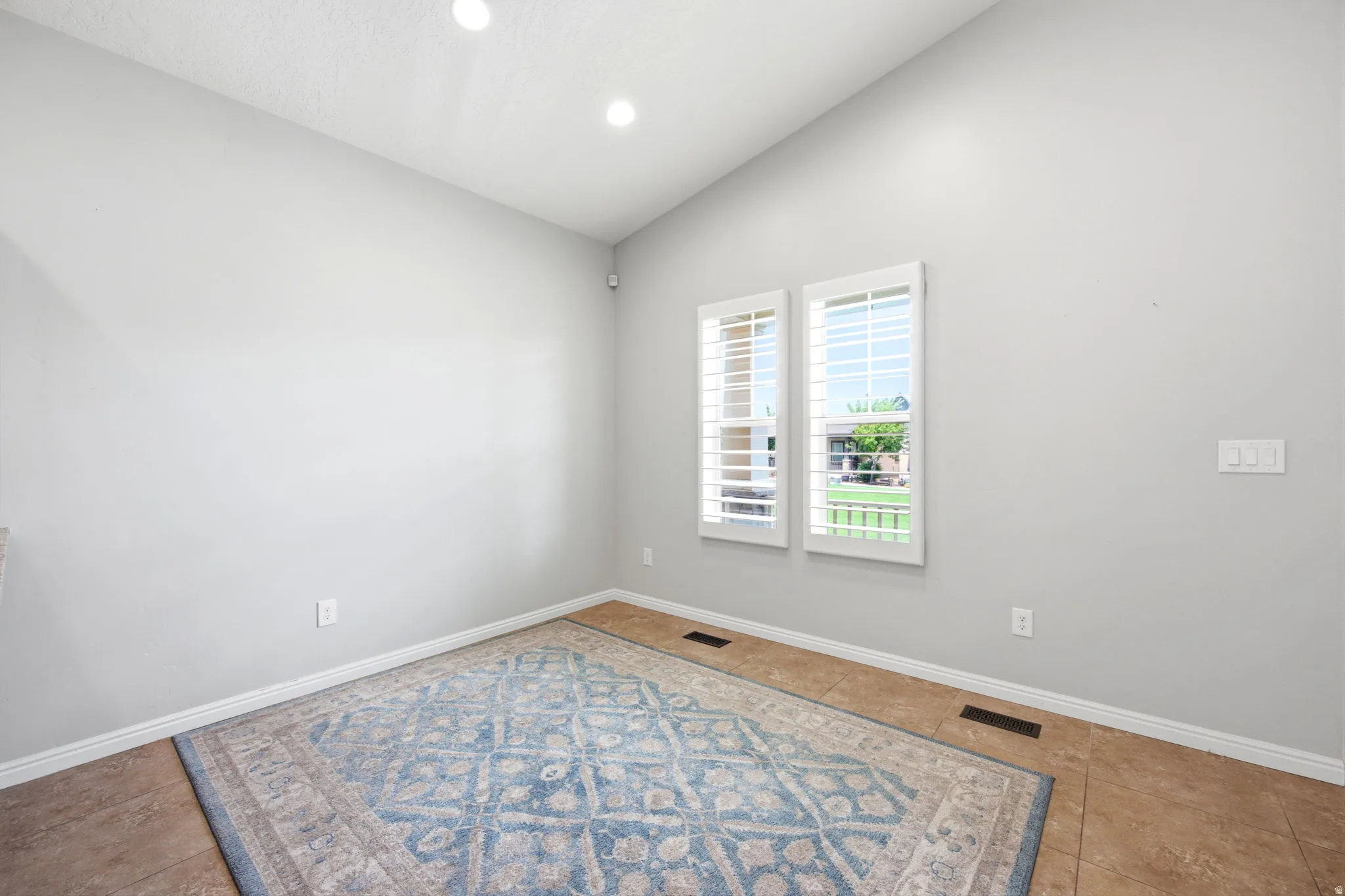 Room with light gray walls, two windows with white plantation shutters, and recessed ceiling lighting